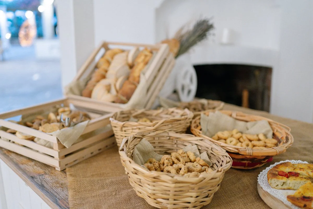 Assorted cookies in wicker baskets and a tray of pizza on a wooden table in a cozy indoor setting.