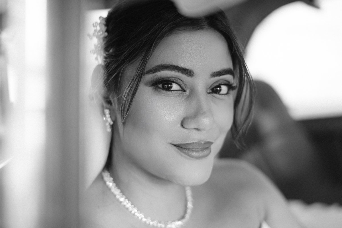A woman with makeup and jewelry smiling and looking at the camera in a car.