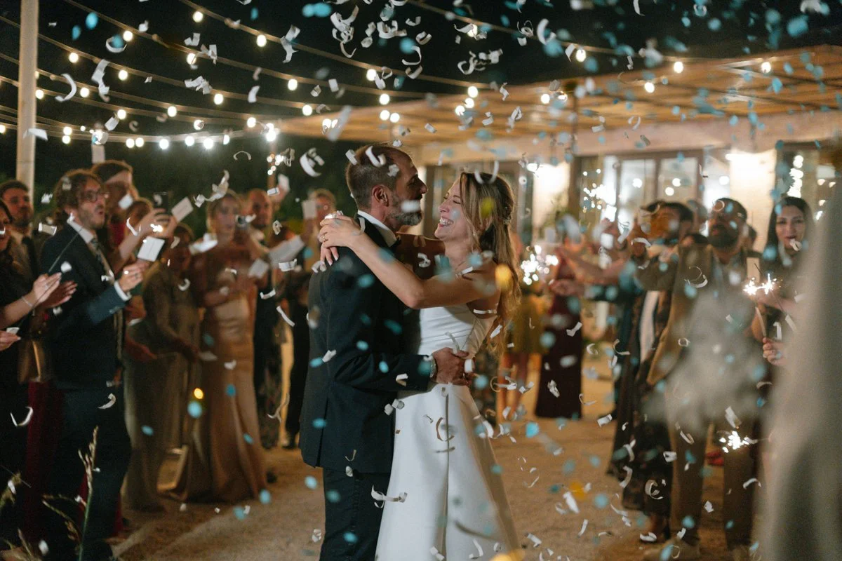 Couple dancing and celebrating with confetti and string lights overhead at a wedding reception.