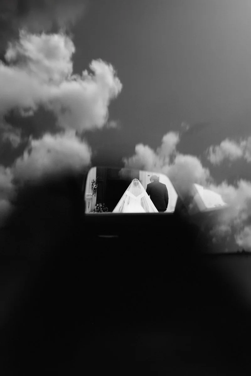 View through a small opening showing a person in formal attire and a wedding tent with clouds in the sky.