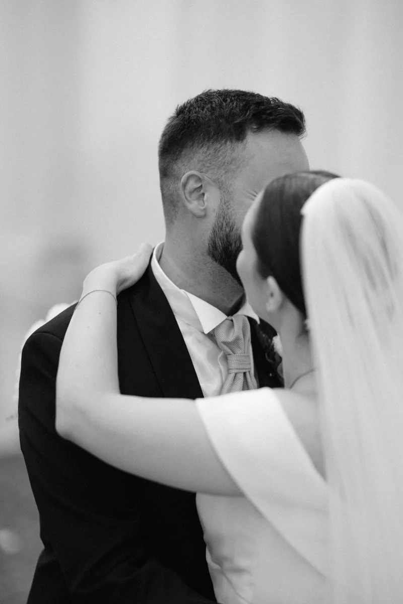 Black and white photo of a bride and groom sharing a kiss, with the bride's arms around the groom's neck.