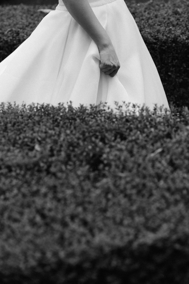 Person wearing a white dress standing behind a hedge