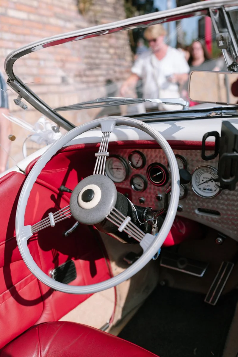 Close-up of a vintage car's dashboard and steering wheel with people in the background.