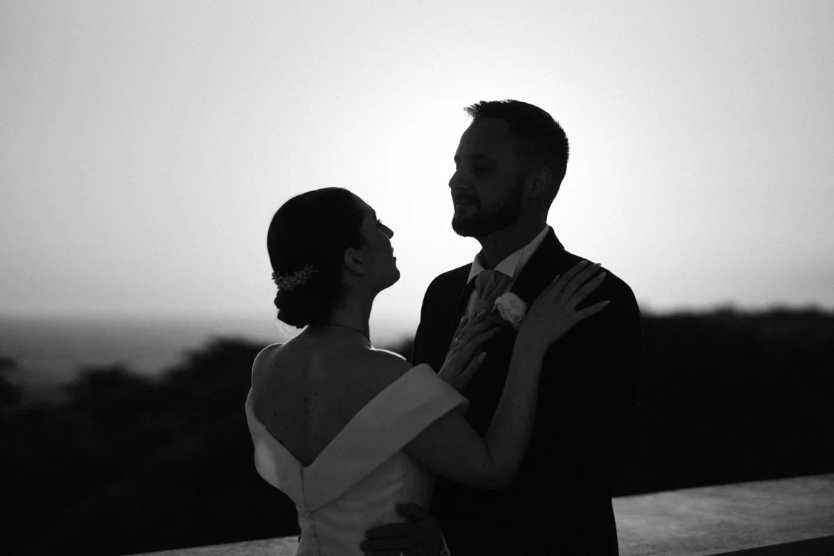 Silhouette of a bride and groom dancing together outdoors at sunset, black and white photo.