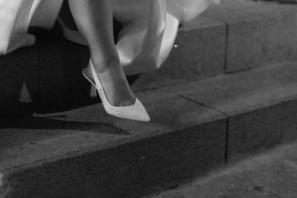 Close-up of a woman's foot in a decorated high heel shoe, resting on a concrete step.