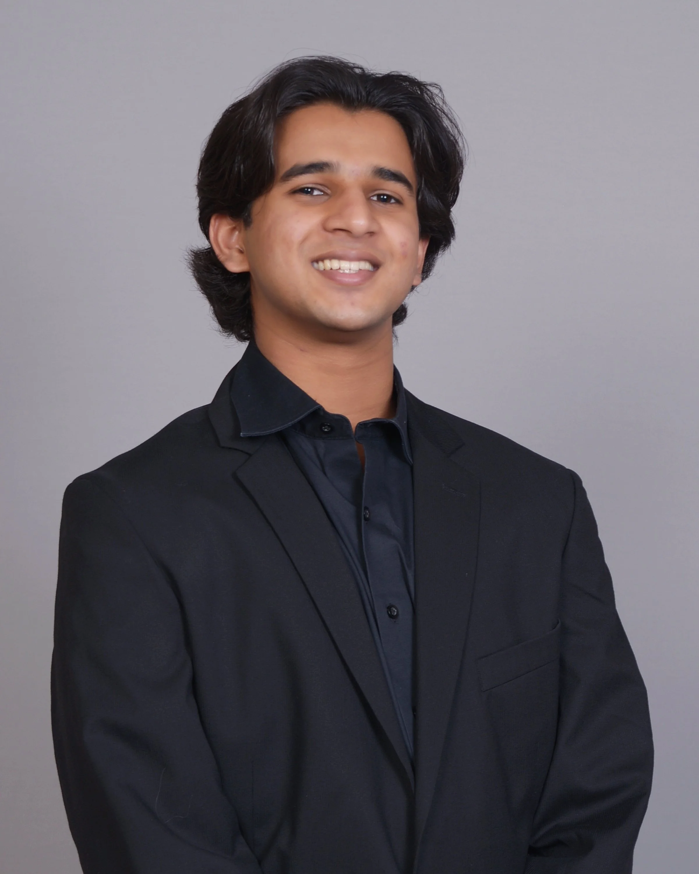 Picture of Ishaan smiling at the camera in a black blazer on a light grey background.