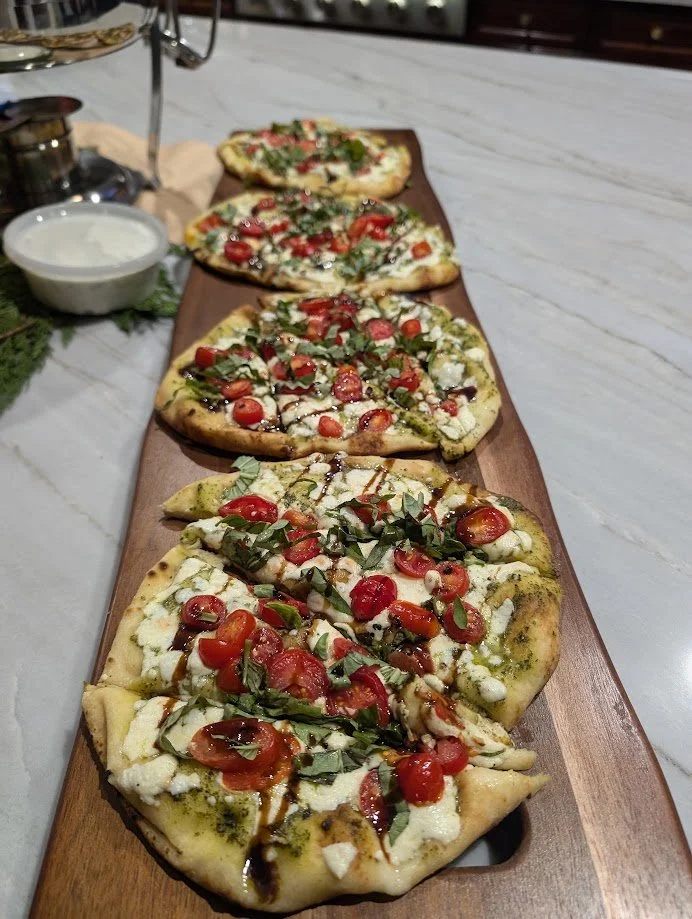 Five individual pizzas with cherry tomatoes, fresh basil, mozzarella, and drizzle of balsamic vinegar on a wooden serving board.