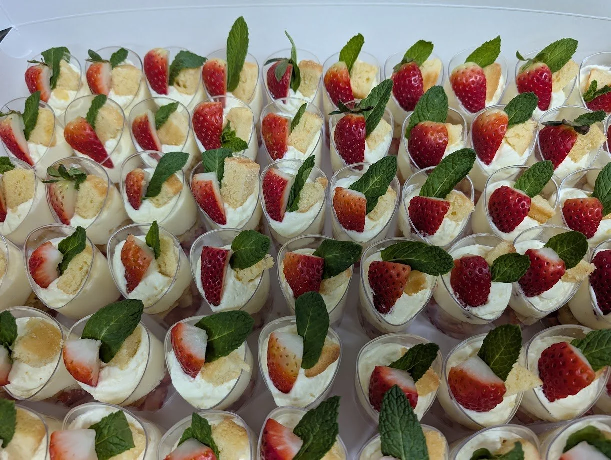 Small dessert cups filled with cream, topped with sliced strawberries, pieces of sponge cake, and fresh mint leaves.