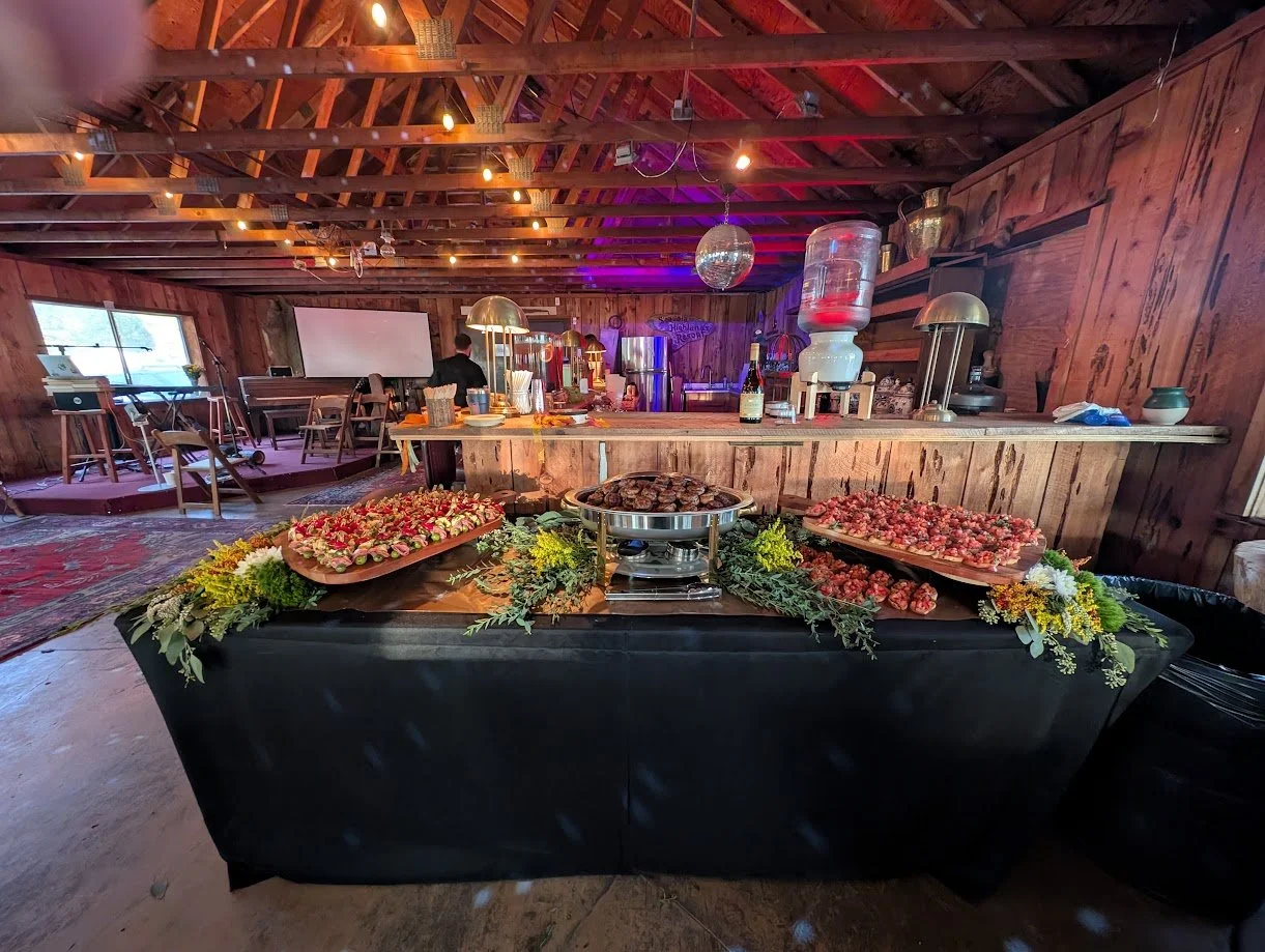 Food table with strawberries and chocolates, decorated with greenery and yellow flowers, in a rustic barn setting with string lights and a dance floor area.