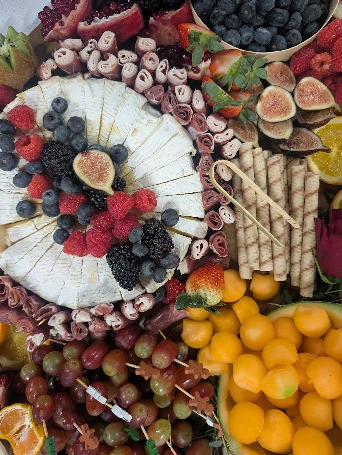 A platter of assorted fruits, cheeses, and rolled deli meats, including blueberries, strawberries, figs, grapes, raspberries, blackberries, and orange slices, along with cheese wedges and sliced cured meats.