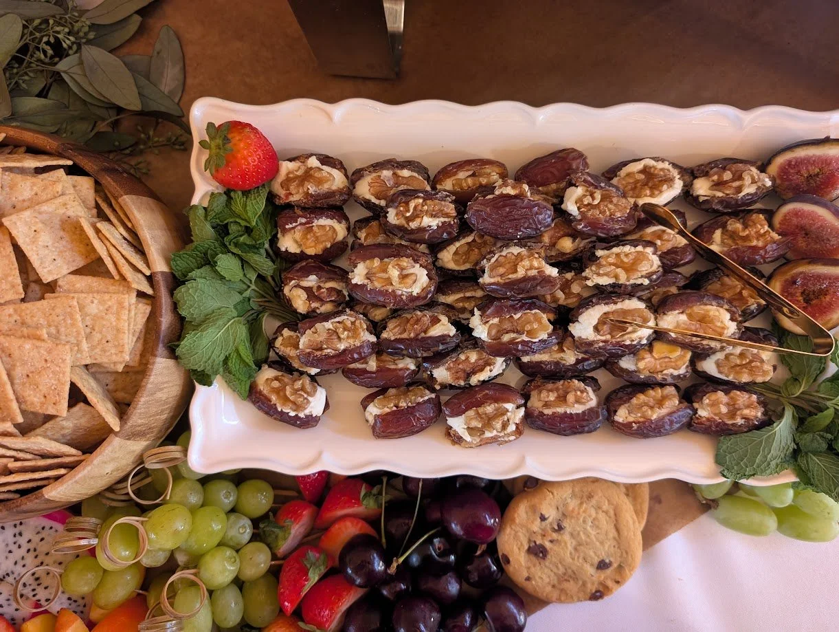 A platter of stuffed dates topped with walnuts, garnished with a strawberry, and surrounded by grapes, strawberries, cherries, and a chocolate chip cookie.