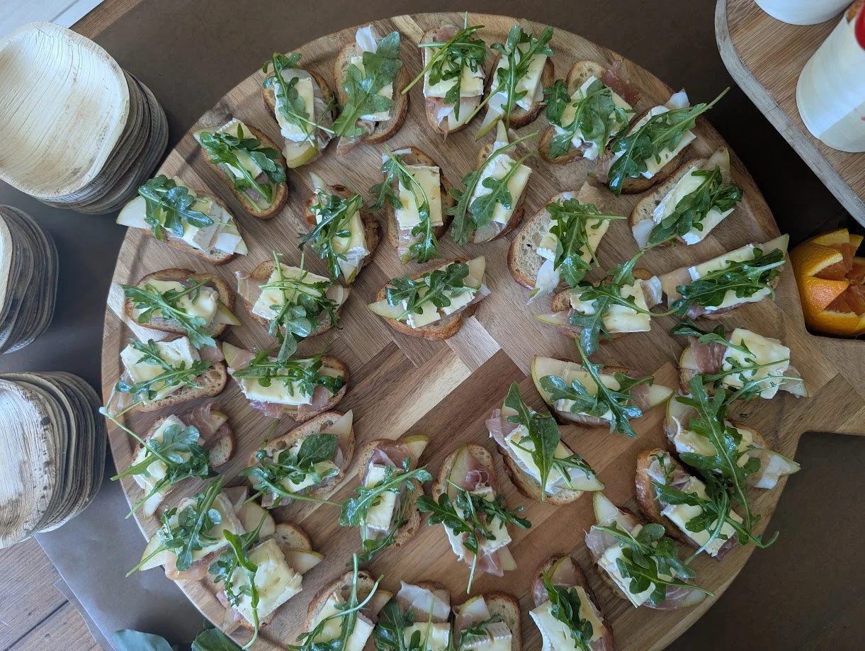 Assorted bruschetta appetizers topped with cheese, prosciutto, and arugula, arranged on a round wooden serving tray.
