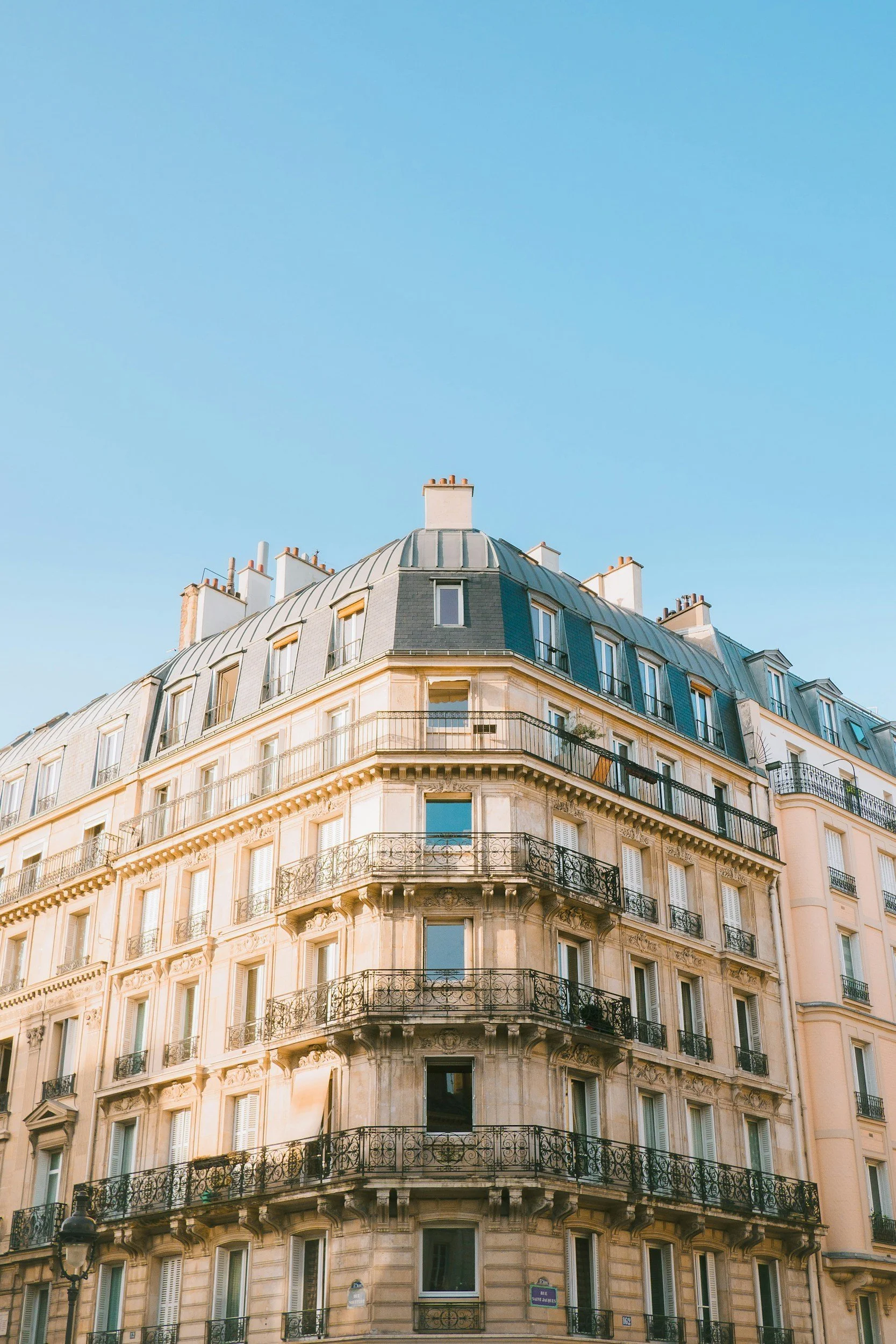 A curved beige Parisian building with wrought iron balconies under a clear blue sky.