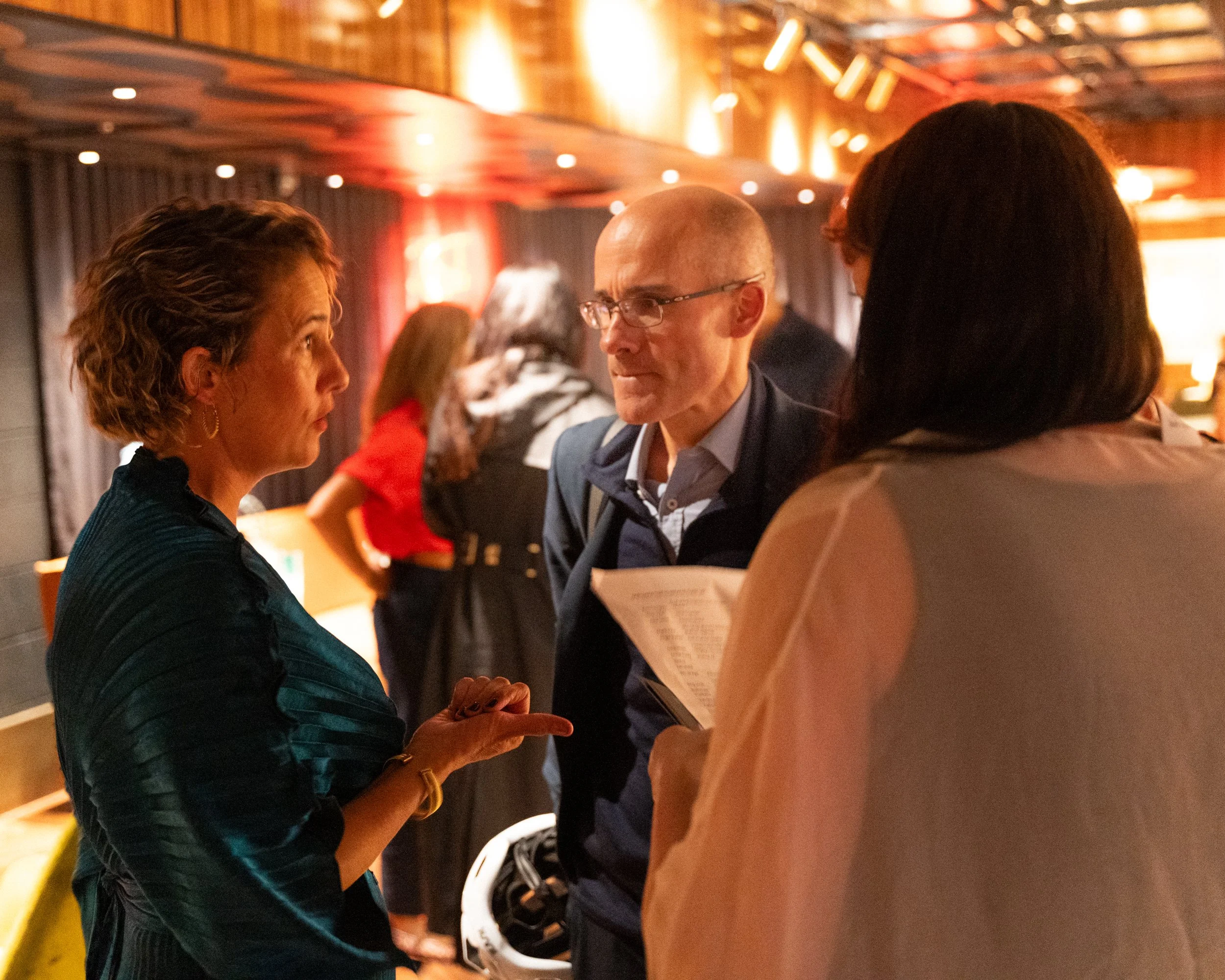 Three people engaged in conversation at a social gathering, with a warm, dimly lit background.