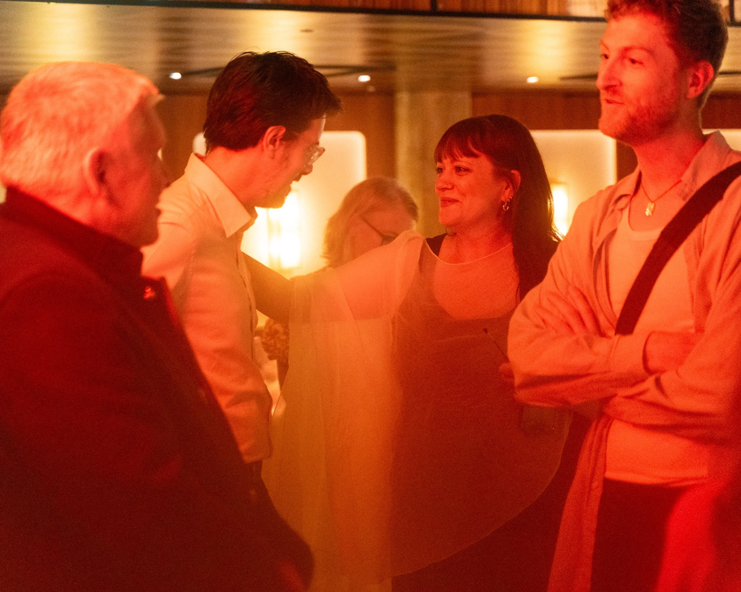A group of people socializing indoors in a dimly lit setting with warm lighting.