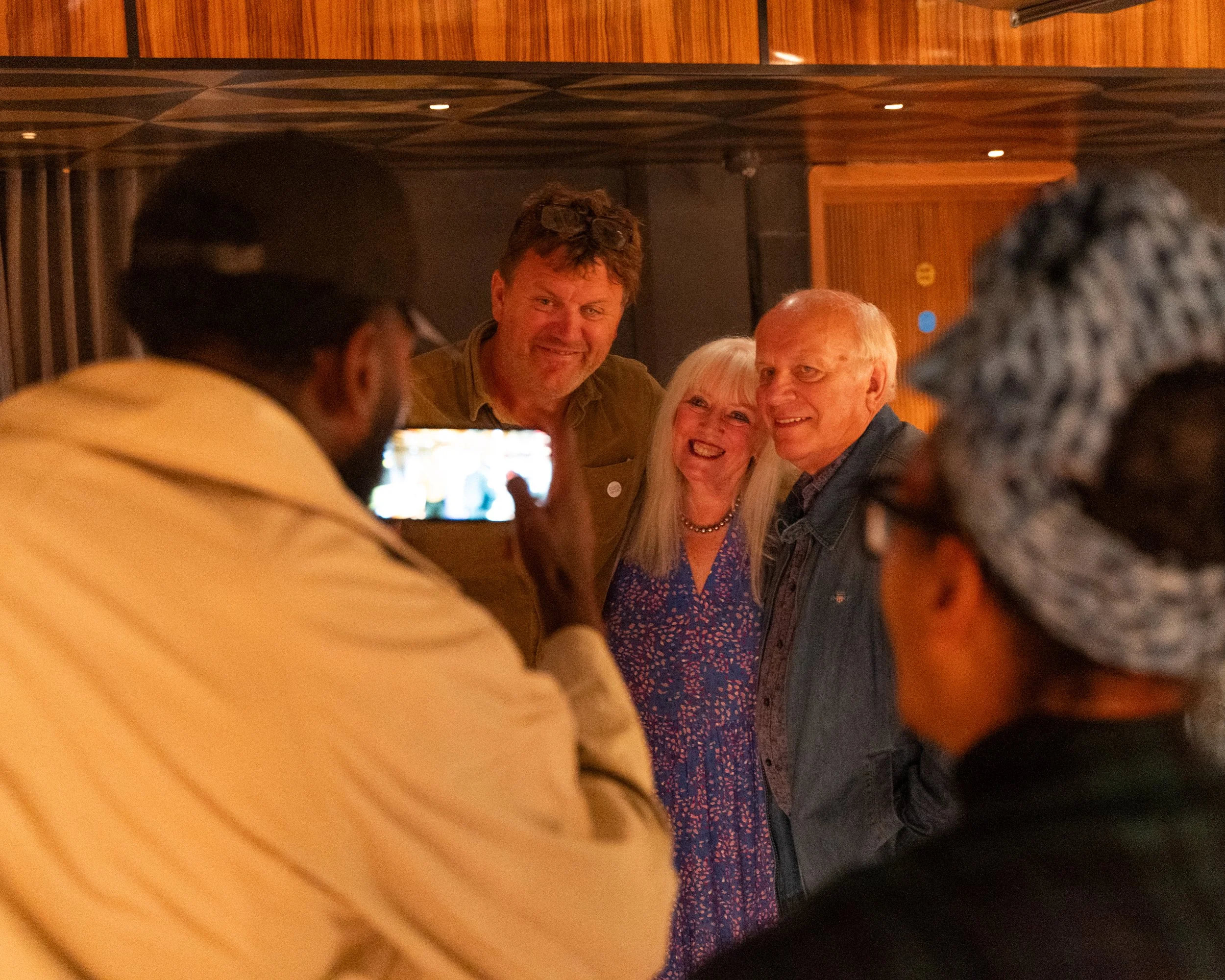 People taking a group selfie in a social setting, smiling and gathered closely together.