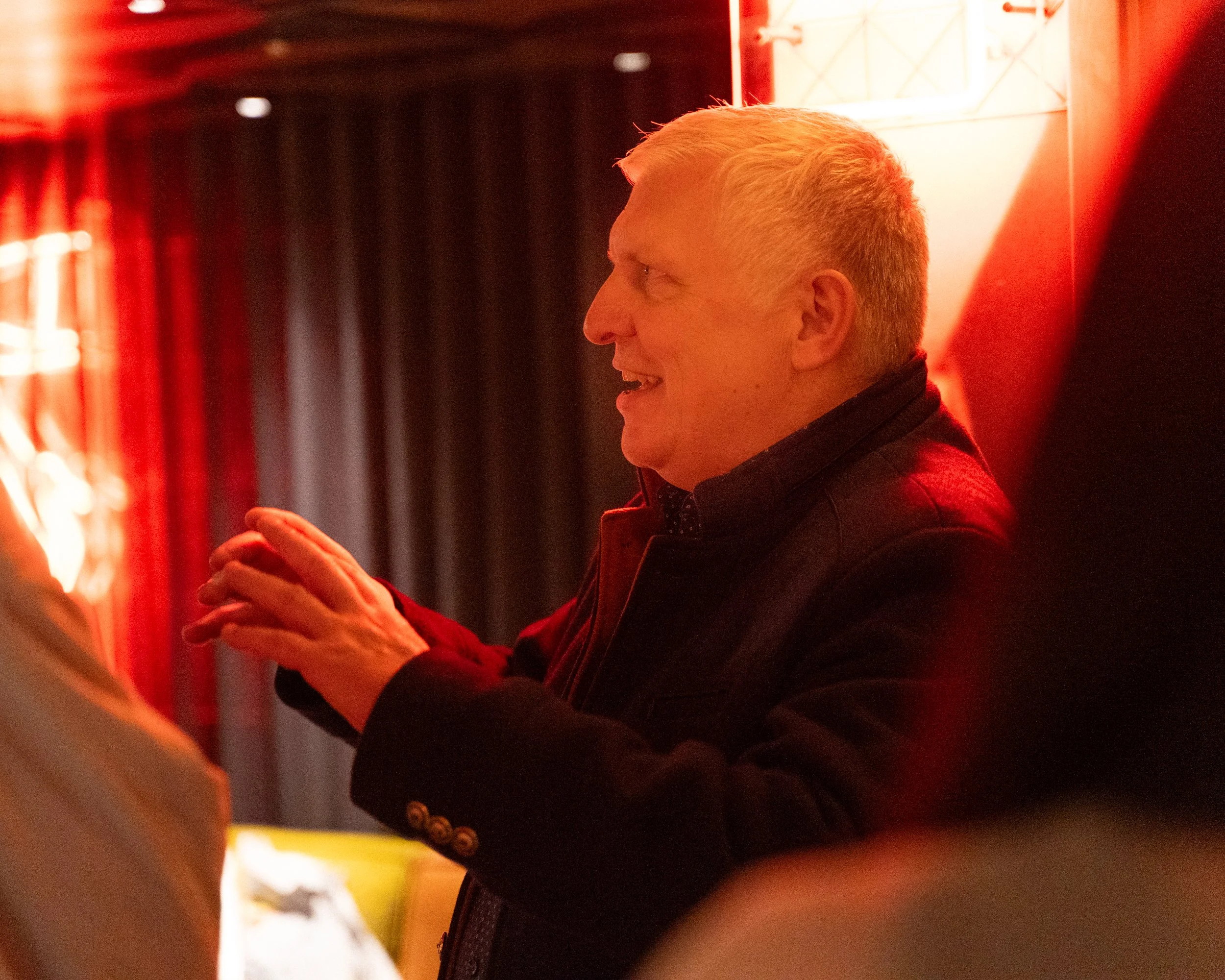 A person with blonde hair smiling and looking at a phone, standing in a room with red lighting.