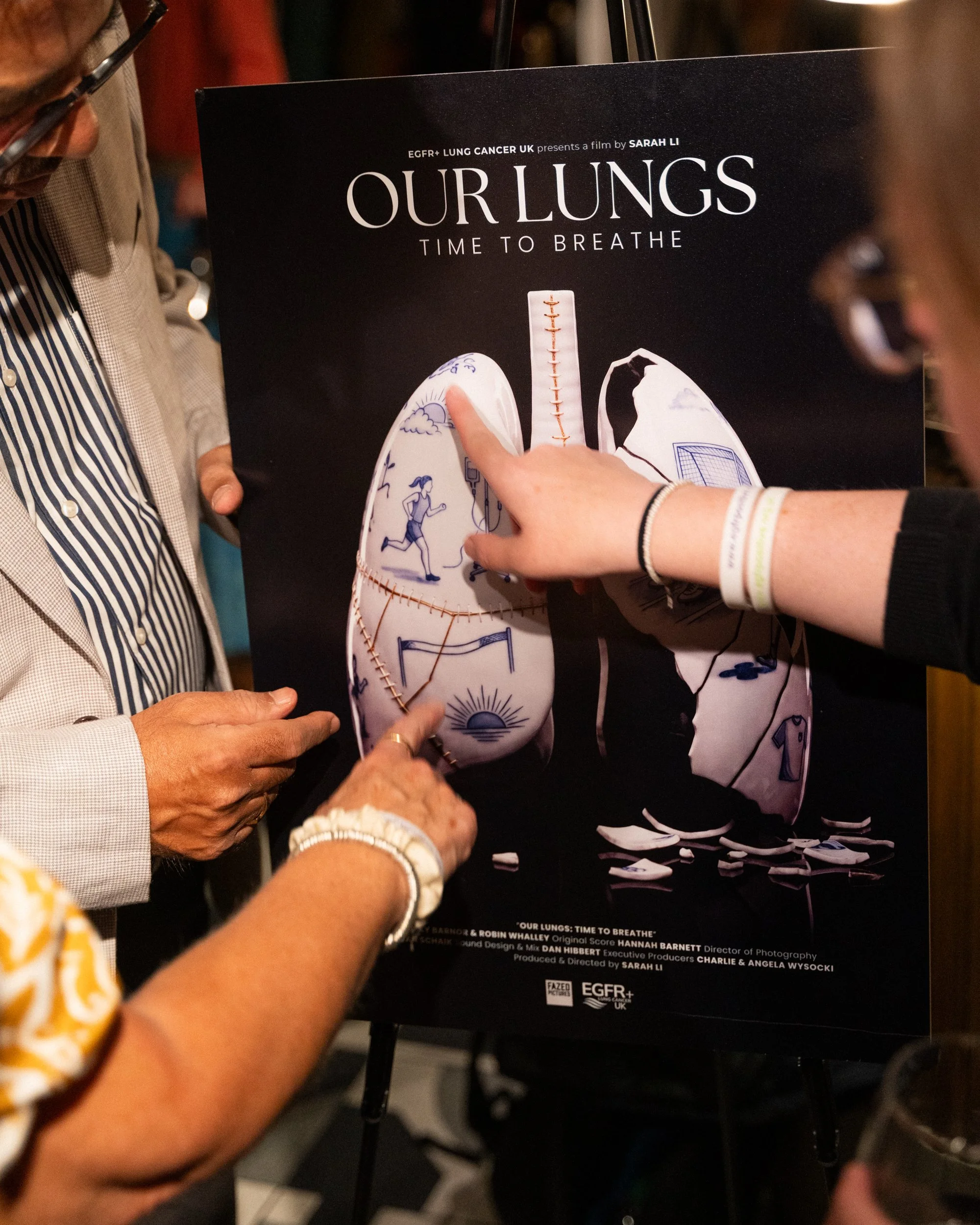 People hold a poster for a film titled 'Our Lungs: Time to Breathe,' which features an illustration of lungs with drawings of a person running and sunshine. The poster includes credits and organizations involved.