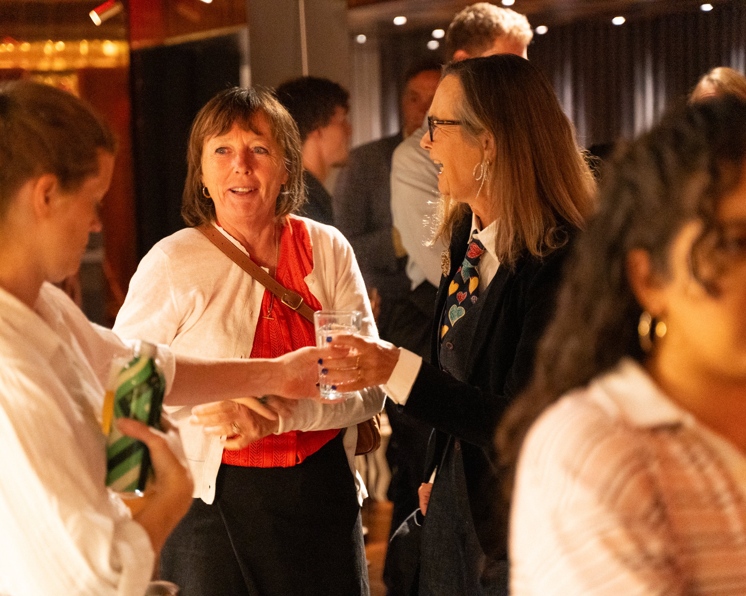 People engaged in conversation at what appears to be a social or networking event in a warmly lit indoor setting.