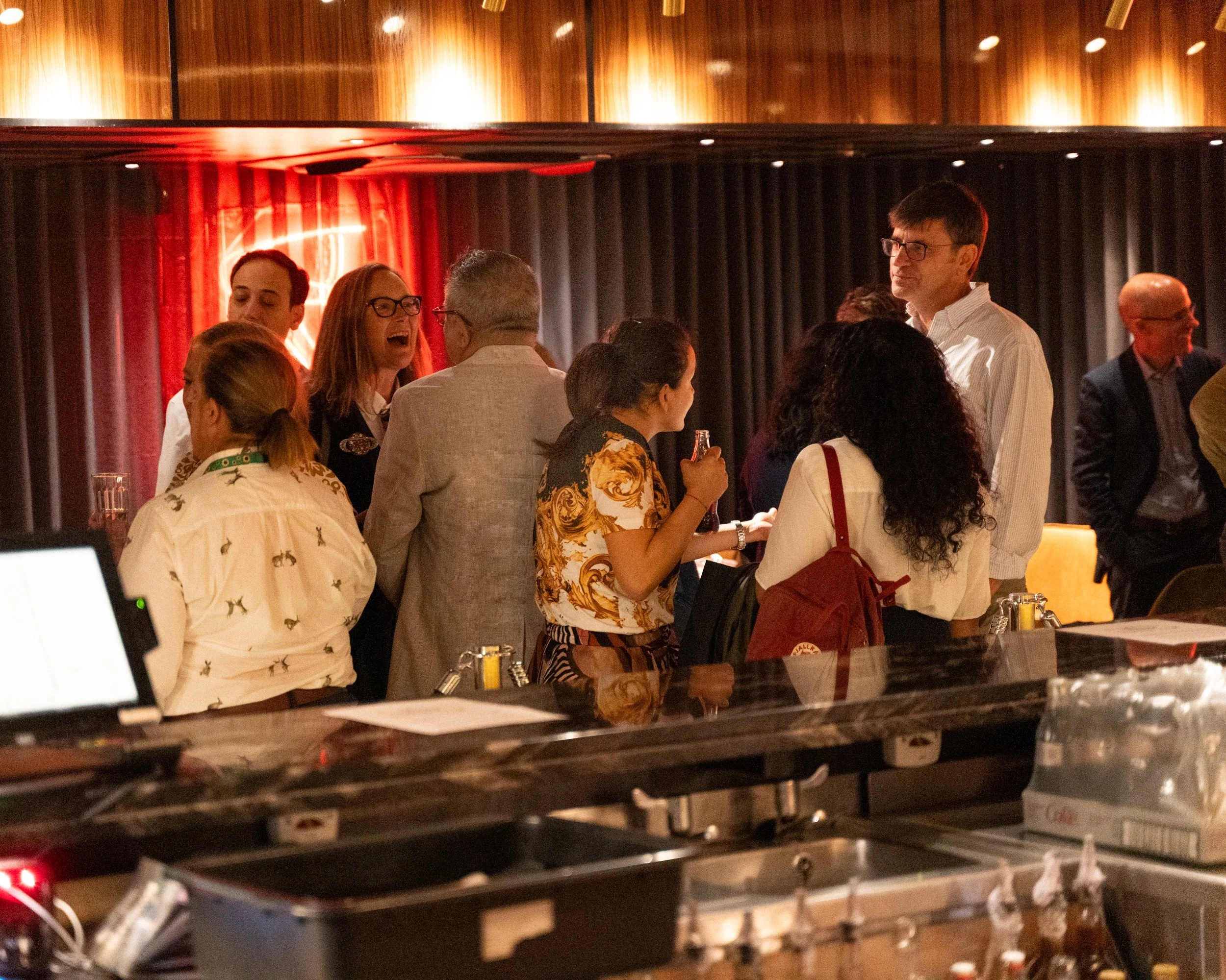 People socializing at a bar or restaurant, with dim lighting and a warm atmosphere.
