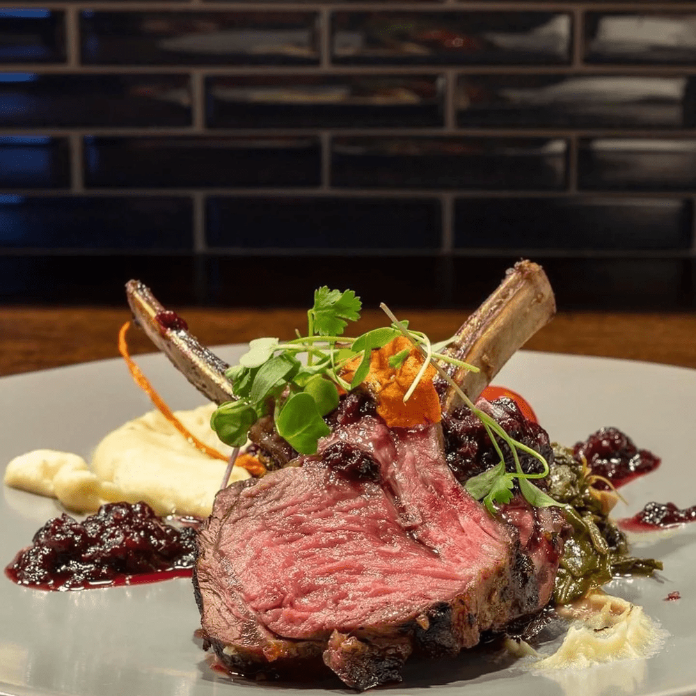 Perfectly cooked lamb chops with creamy purée, vegetables and microgreens, showcasing fine dining services from a private chef.