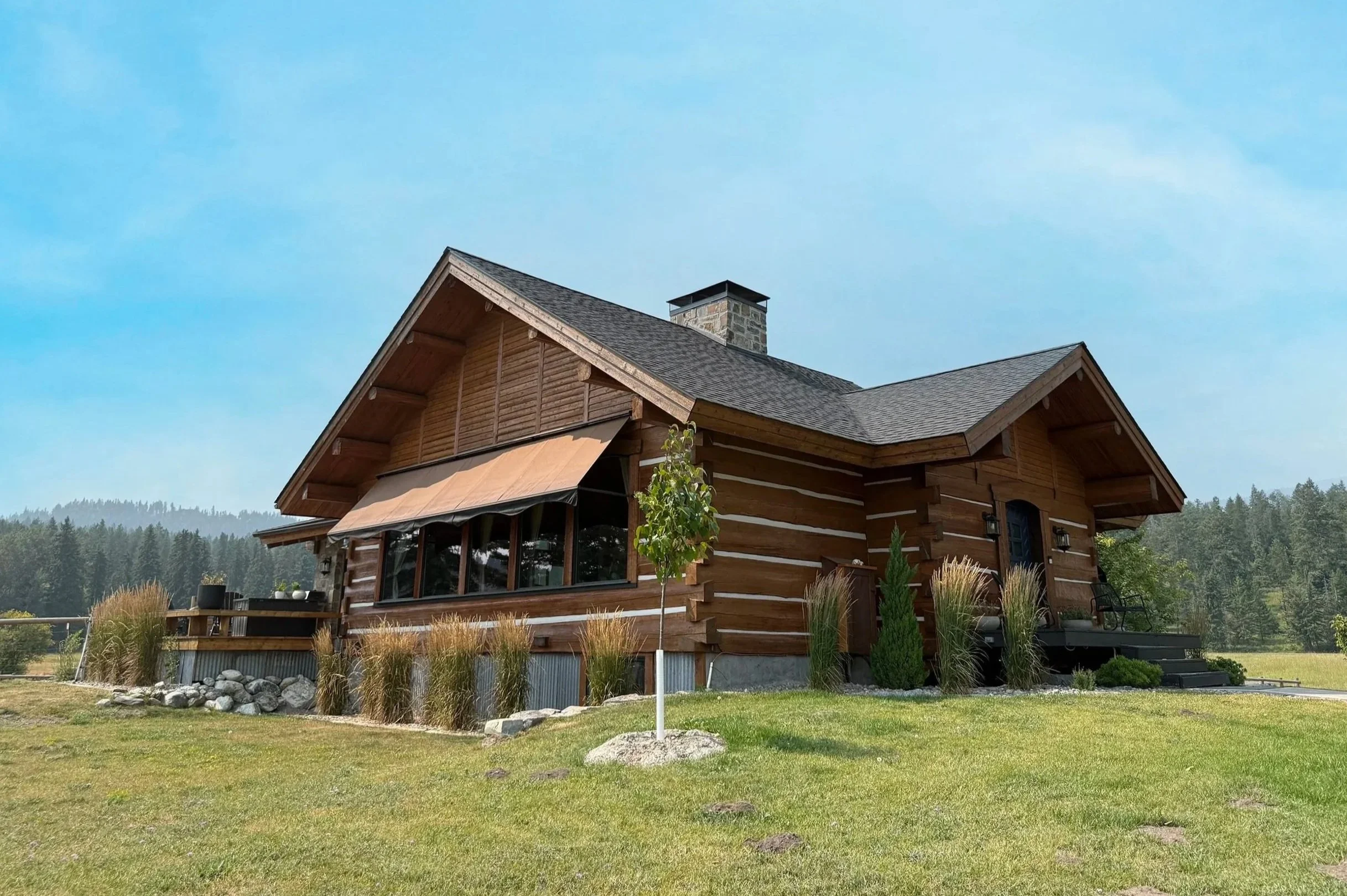 A beautiful, cabin style home set on a grassy field under a bright blue sky.