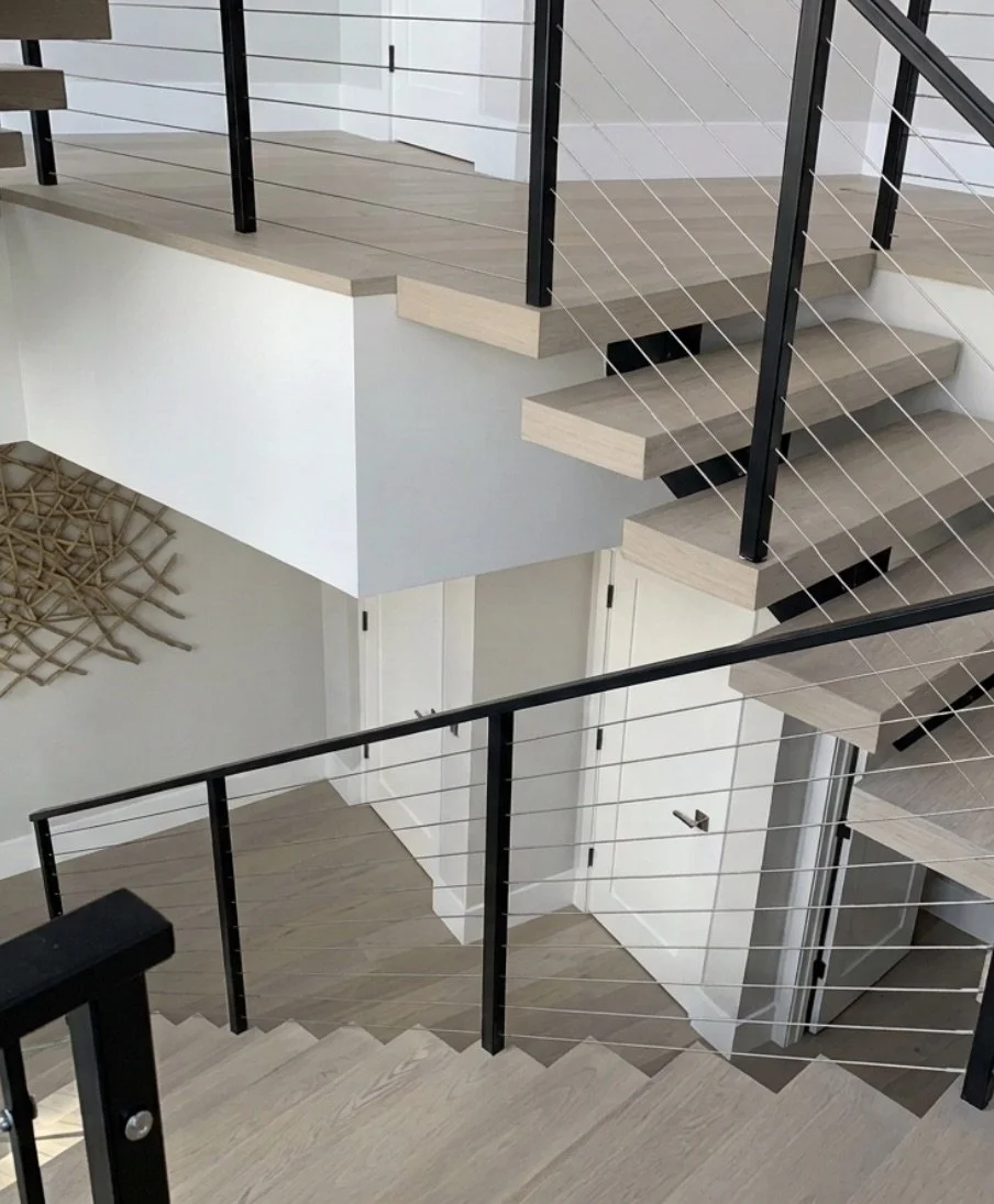 Beautiful, modern two-story floating staircase with contrasting black cable railing and light colored treads.