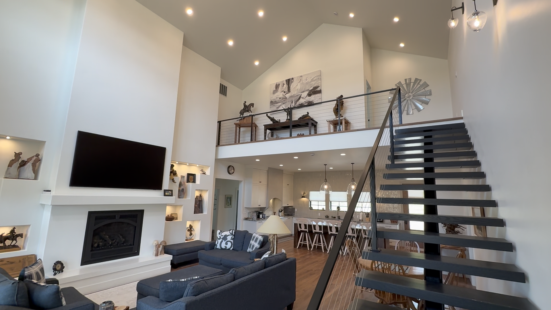 Modern living room with high ceilings, hardwood floors, floating staircase, and fireplace, adorned with rustic decor.