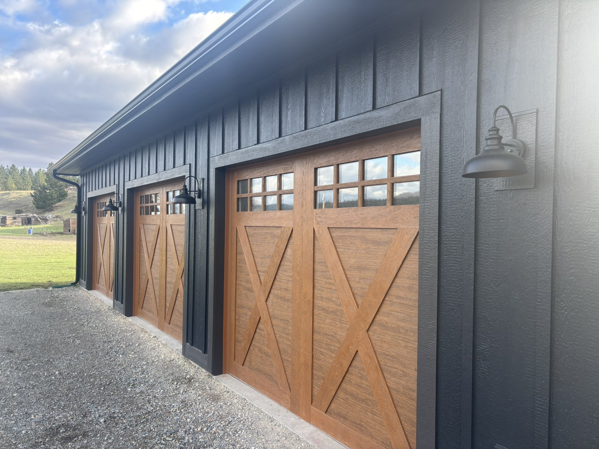 Three wooden garage doors with small windows at the top, set in a black building with exterior lights.