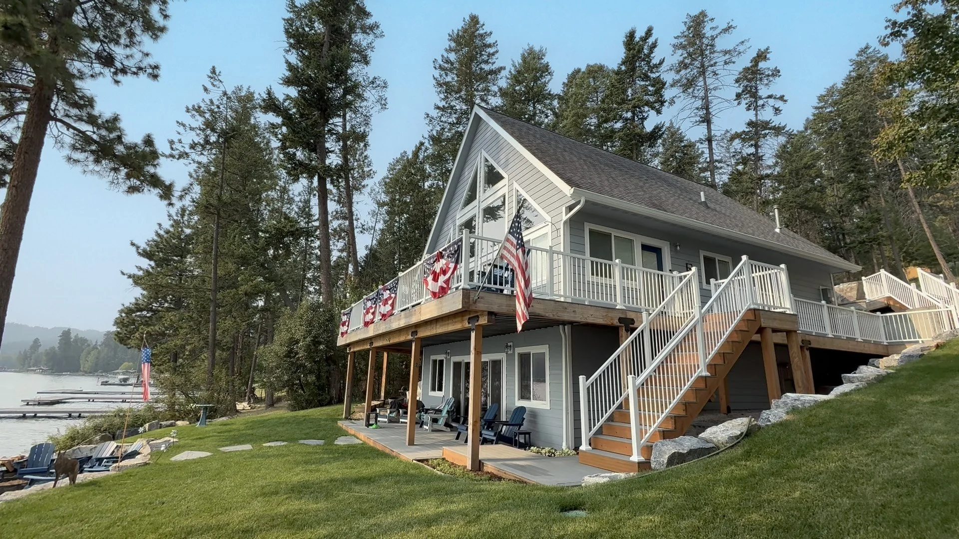 Two-story house with outdoor balcony, blue siding, surrounded by trees, with view of lake.