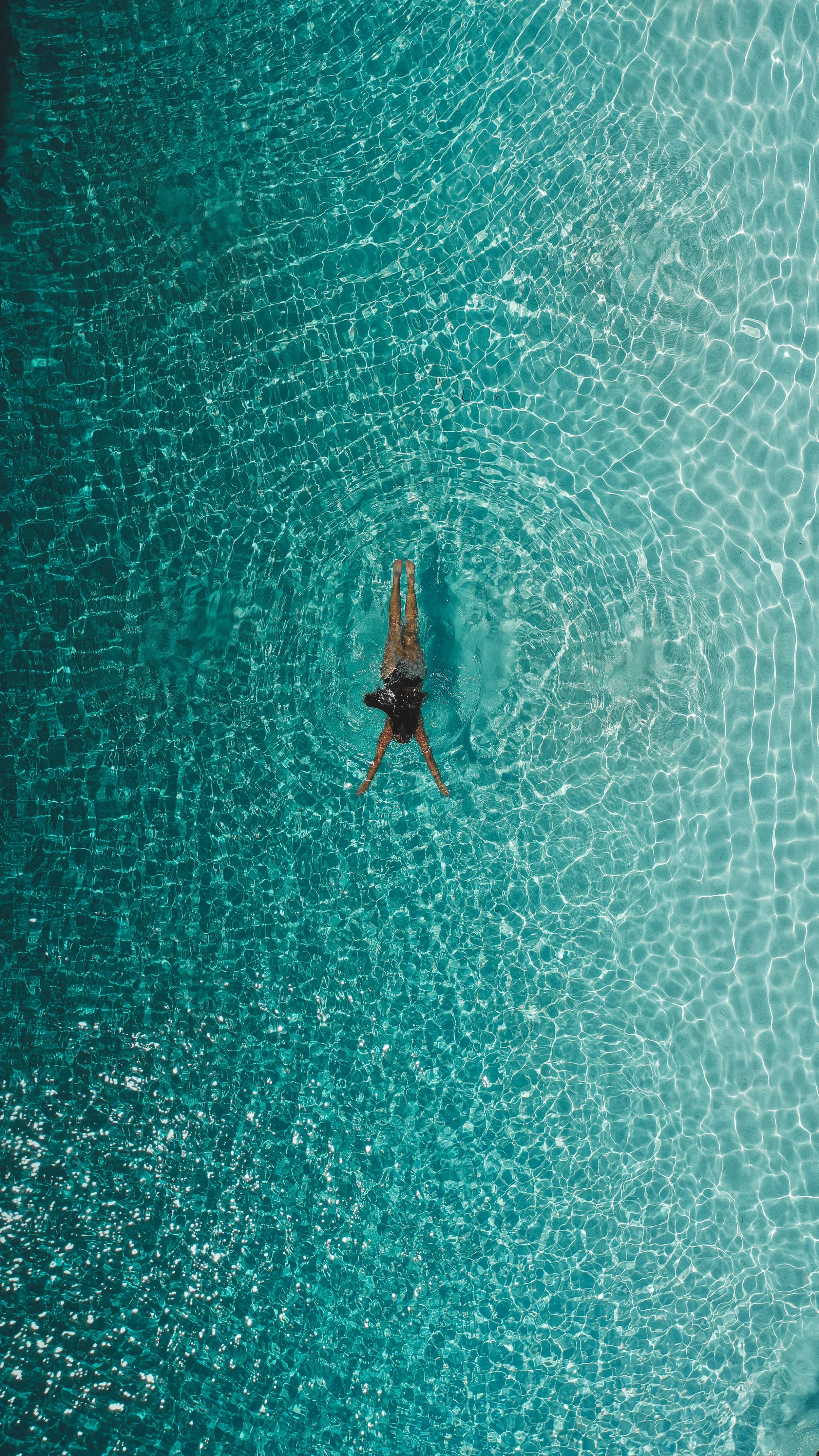 Persona nadando en una piscina de agua cristalina, vista desde arriba.
