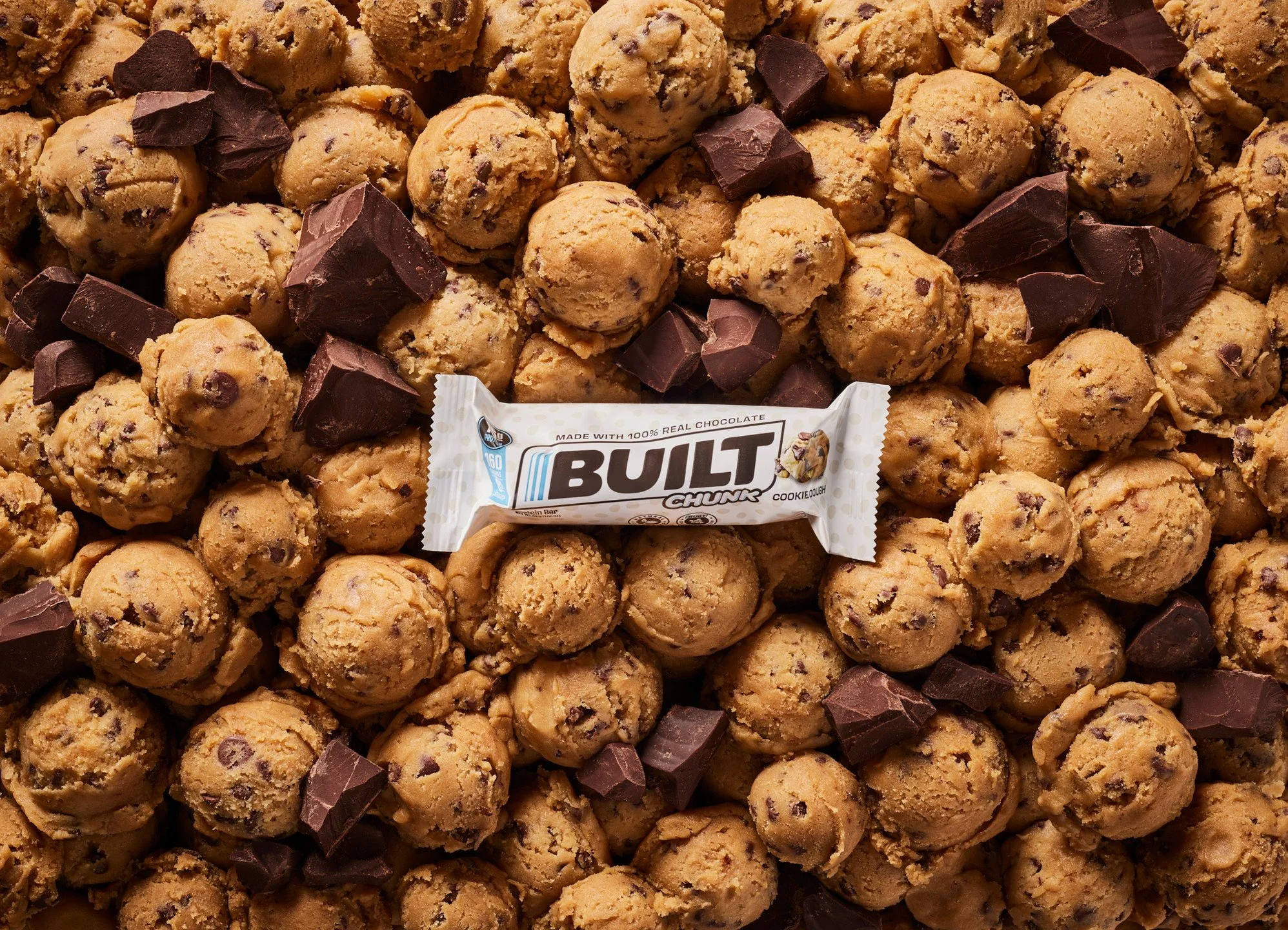 Close-up of a large pile of chocolate chip cookie dough balls with chunks of dark chocolate.