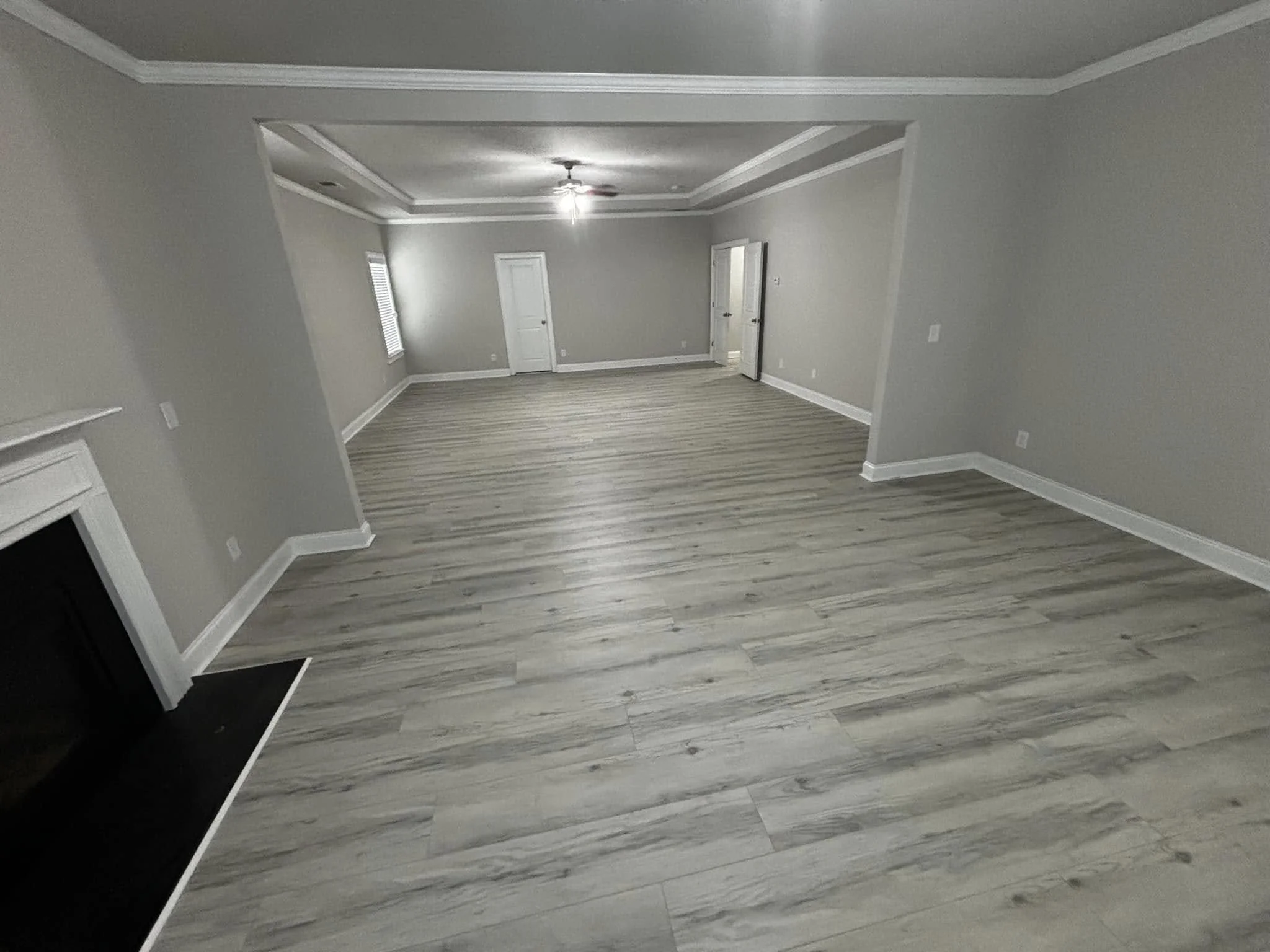 Empty room with light gray walls, a white ceiling with crown molding, a ceiling fan with lights, a window with blinds, a white door, and wood-look flooring.