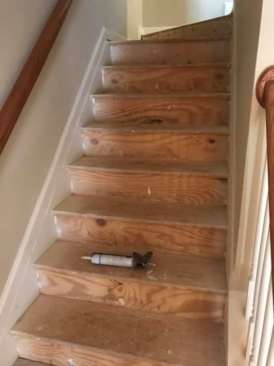 A wooden staircase in a house with a caulking tube and a putty knife placed on one of the steps.