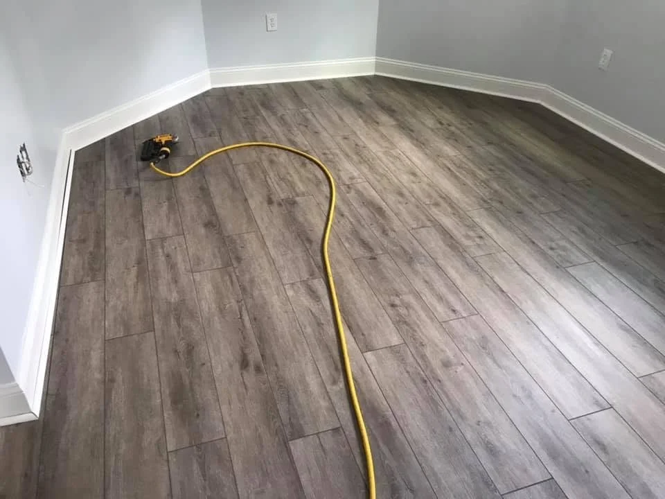 Empty room with wood laminate flooring, gray walls, and a yellow extension cord on the floor.