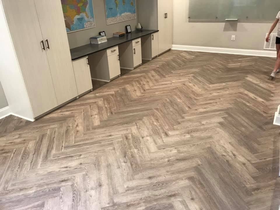 Room with wood-patterned herringbone floor, white cabinets, and maps on the wall.