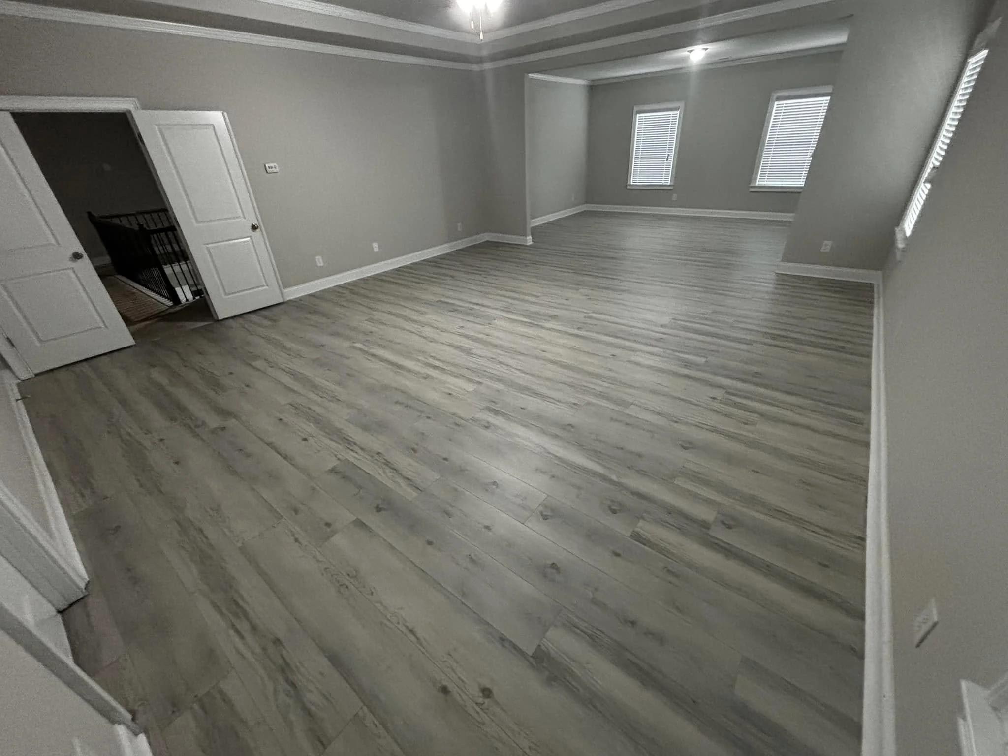 Empty room with light-colored wooden flooring, light gray walls, three windows with blinds, and a ceiling fan with lights.