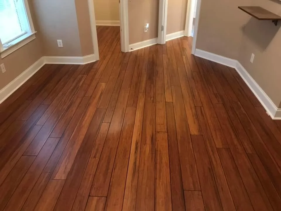 Empty room with polished hardwood floors, beige walls, white baseboards, a window, and a small floating shelf on the wall.