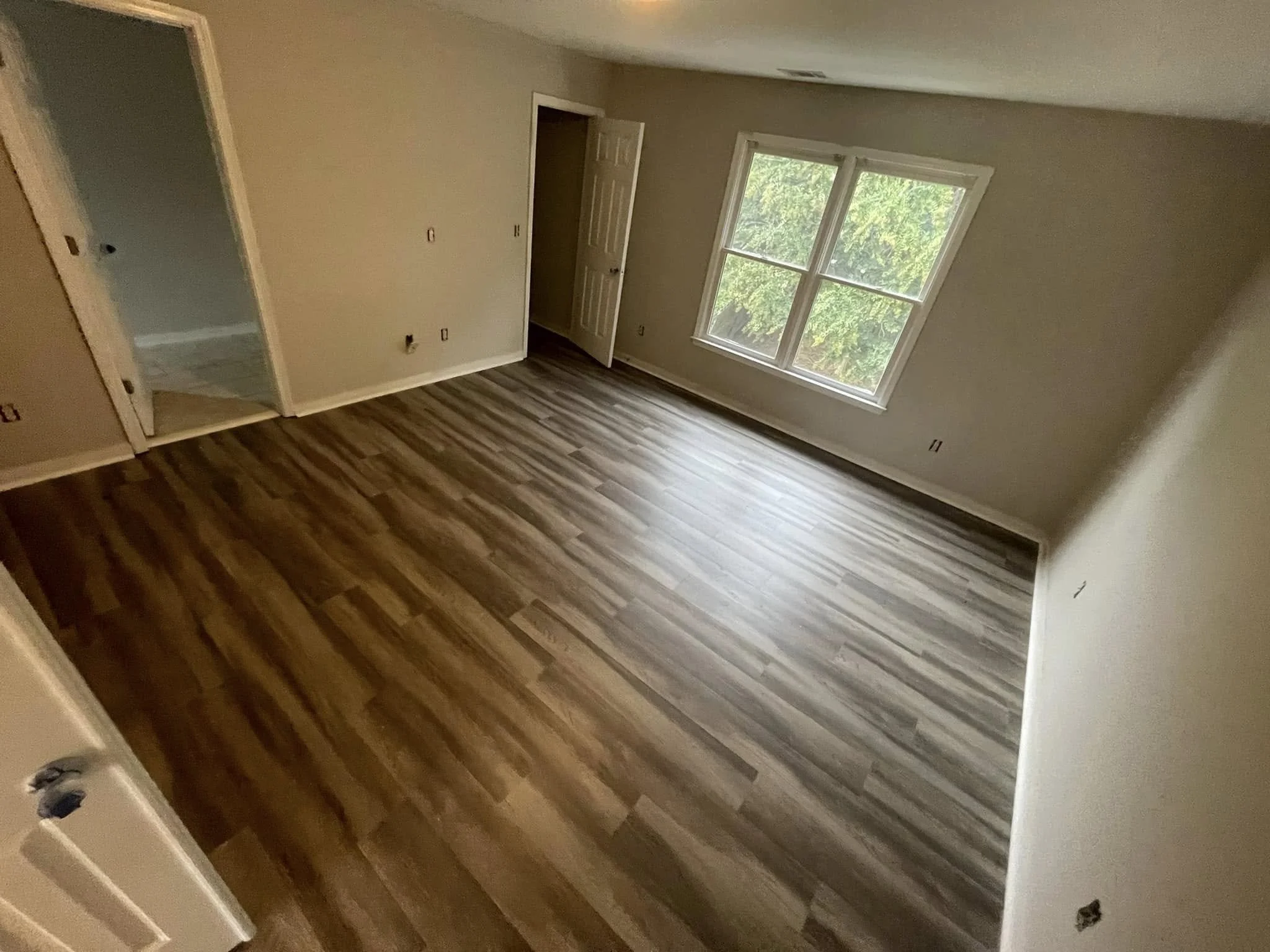 Empty room with hardwood floors, beige walls, double window, and open closet door. Small dog peeking in from bottom left corner.