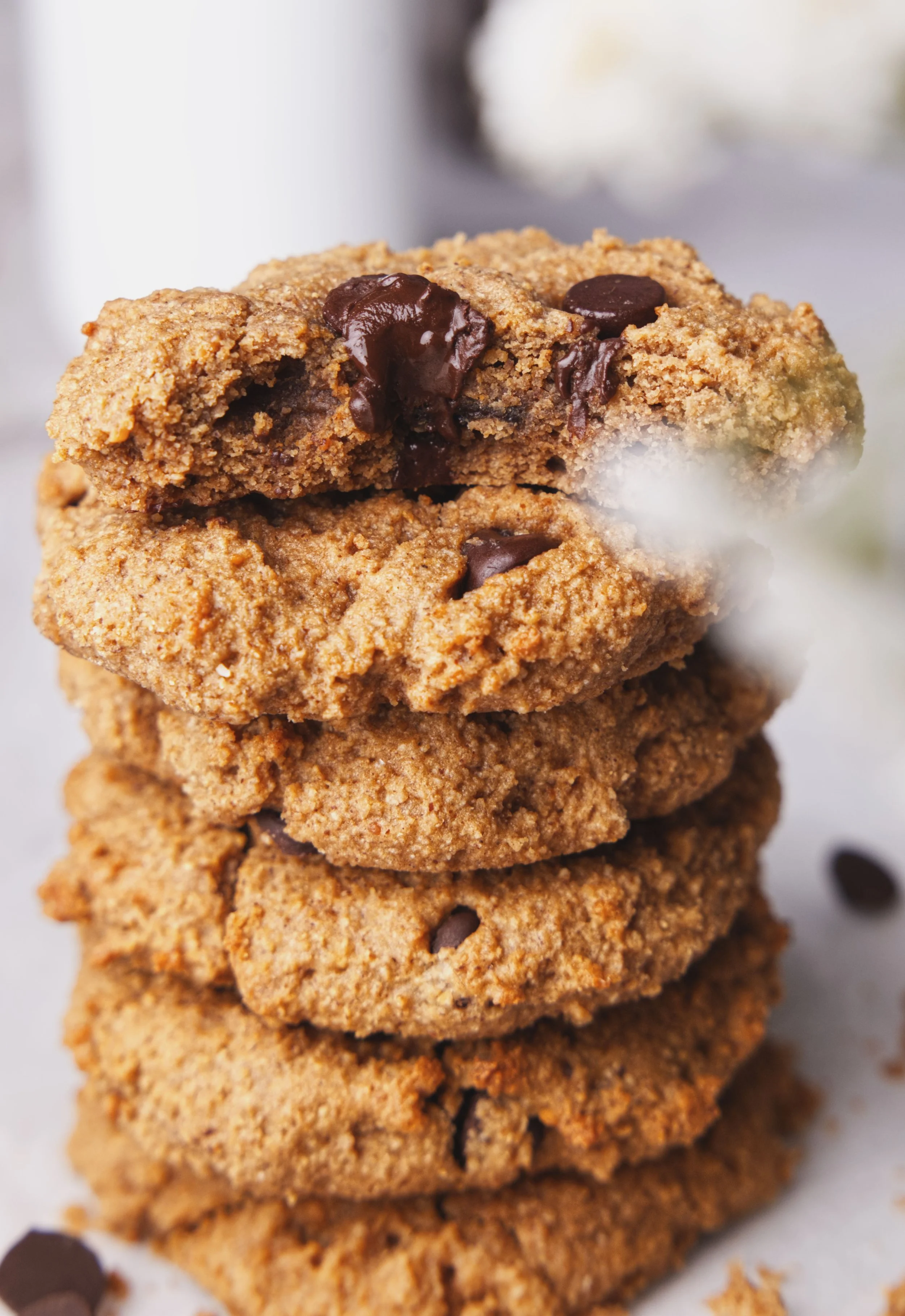 Stack of four chocolate chip cookies with visible chocolate chunks, arranged vertically on a white surface with scattered chocolate chips around.