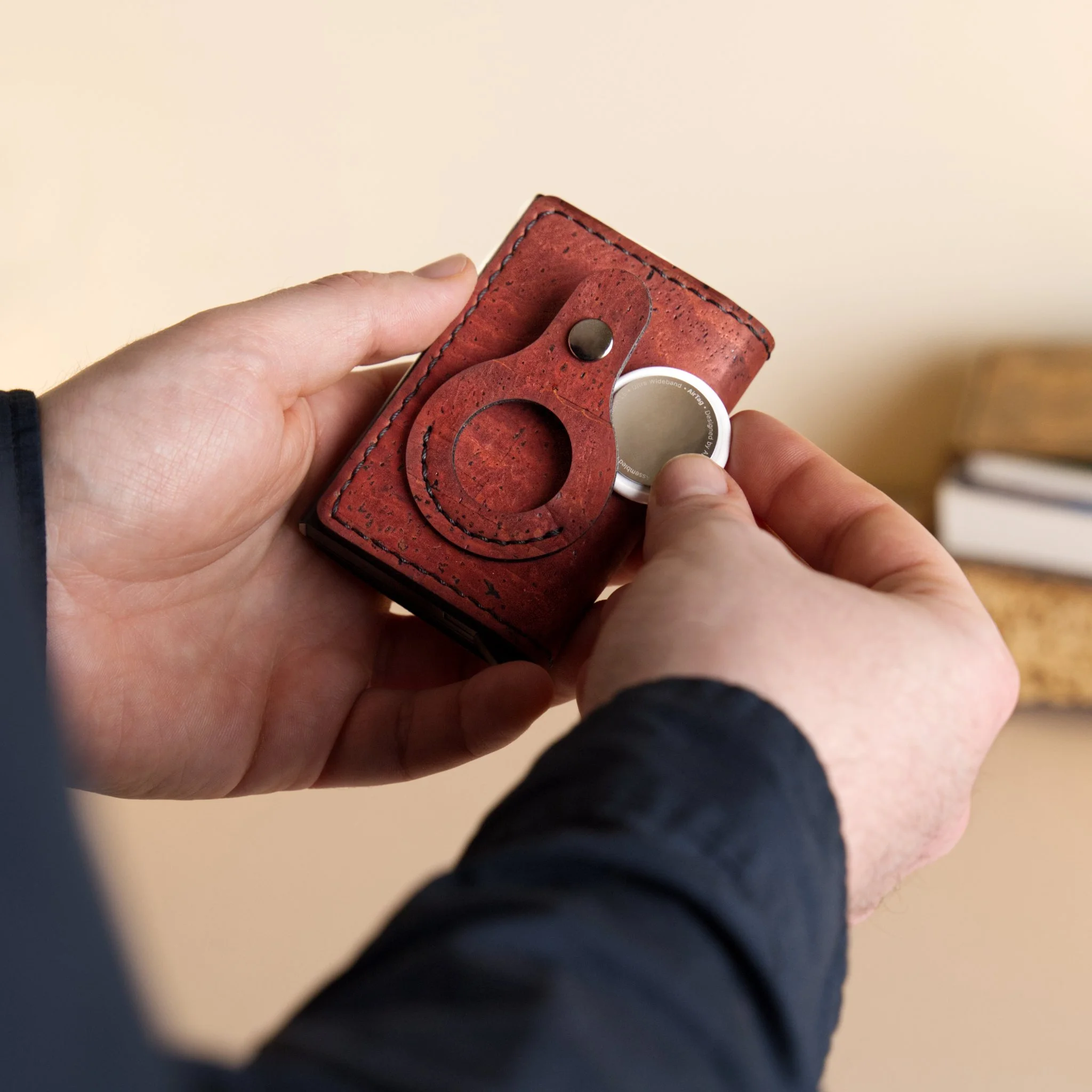A person holding a red leather wallet with a metal snap button and a white circular object inside.