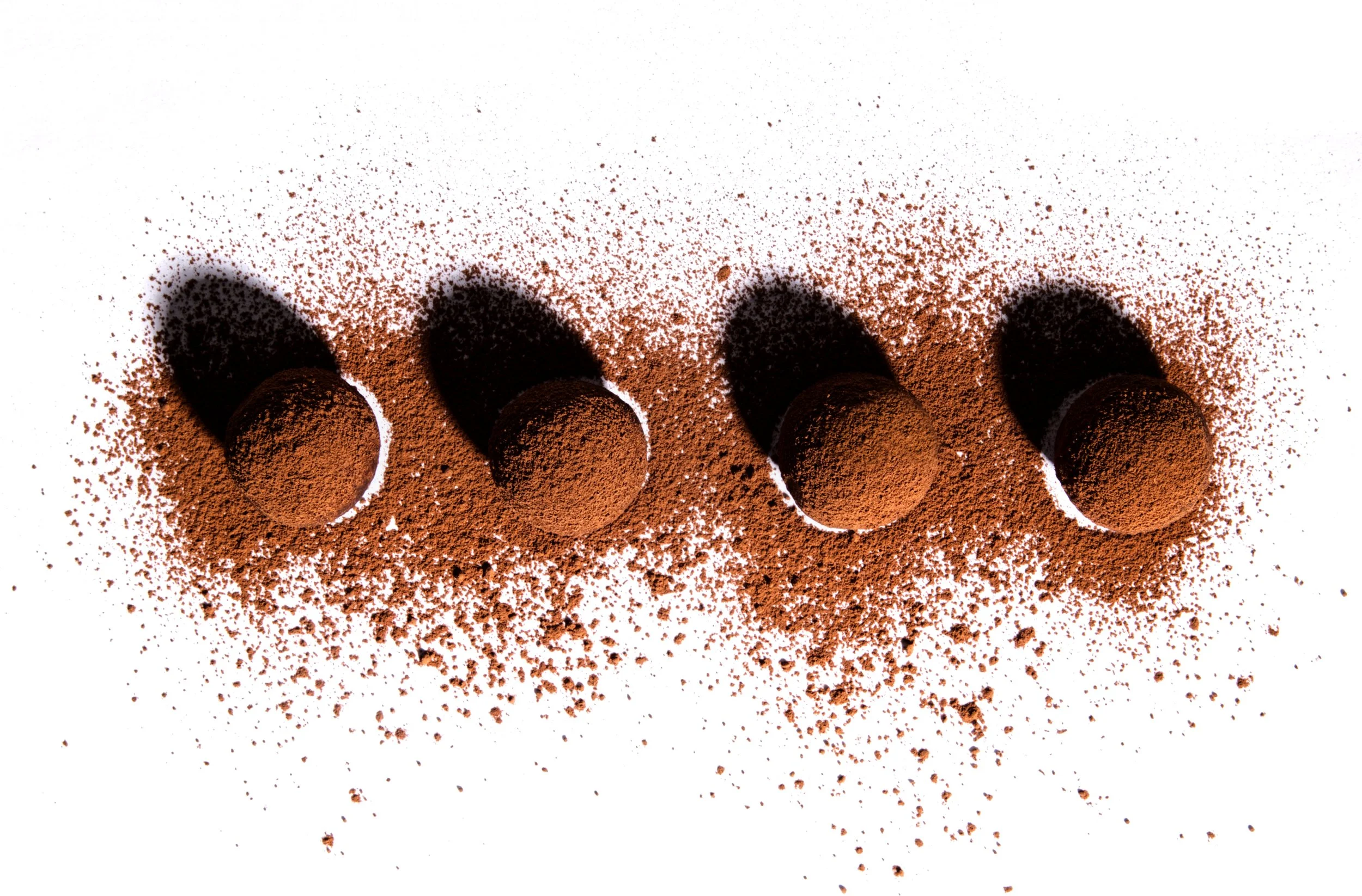 Four spheres coated with cocoa powder aligned on a white surface, with scattered cocoa powder around them.