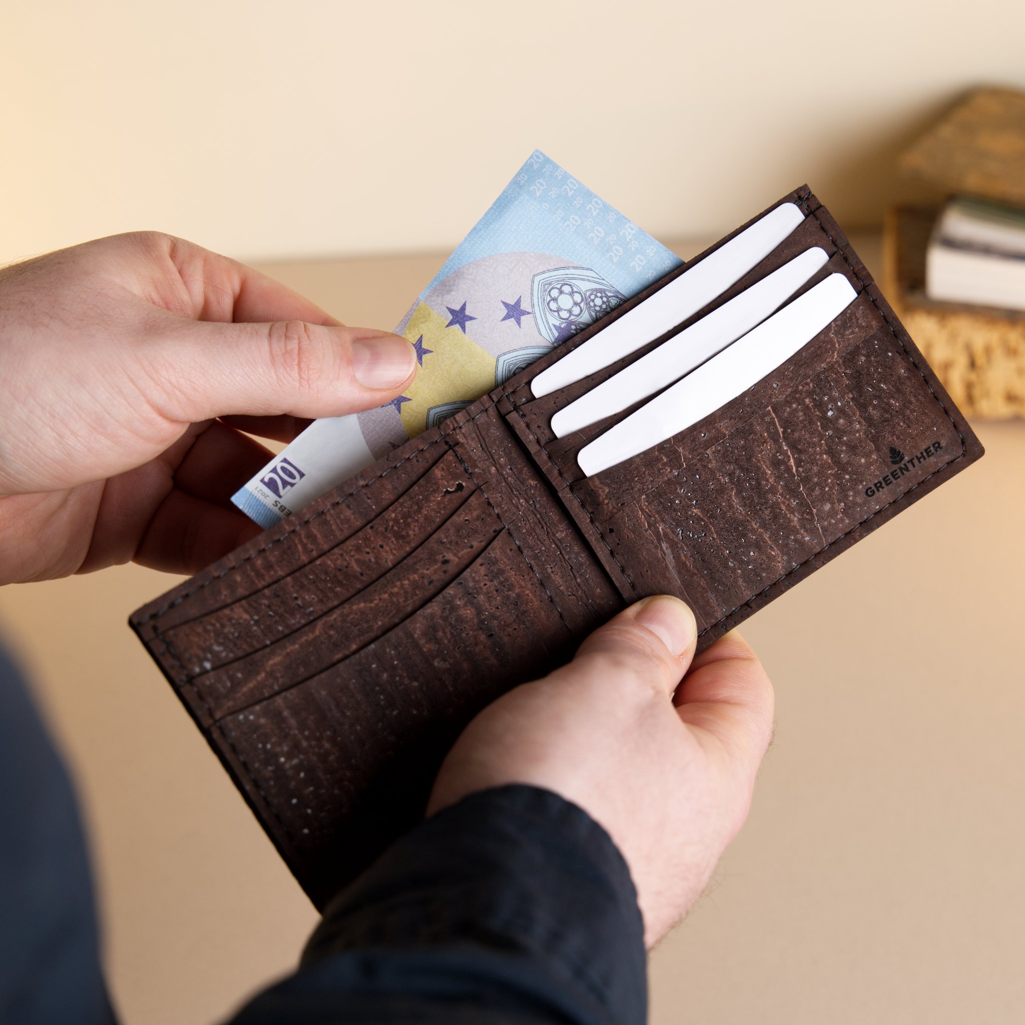 Close-up of a person's hand holding a brown leather wallet with a twenty euro bill partially visible inside.
