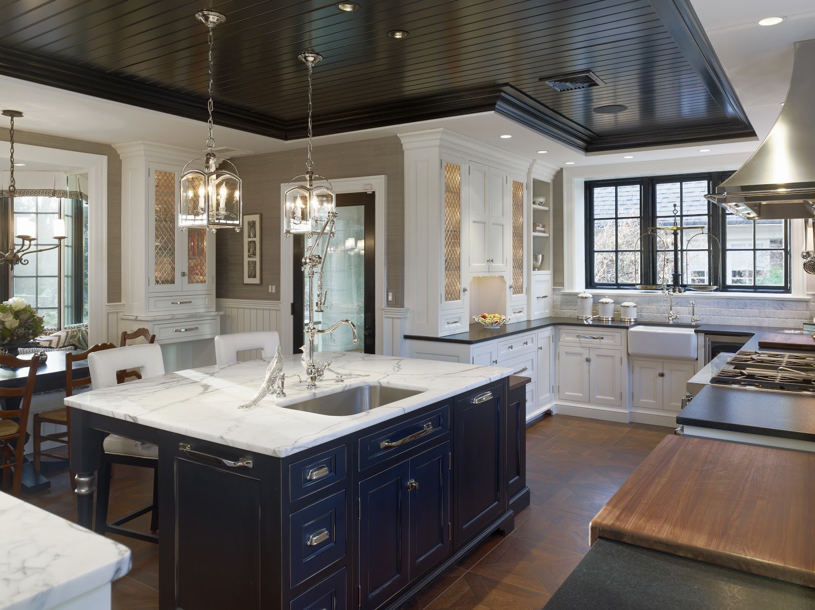 A spacious kitchen with white cabinets, black countertops, and a large island with a marble top. There are pendant lights hanging above the island, and a window over the sink.