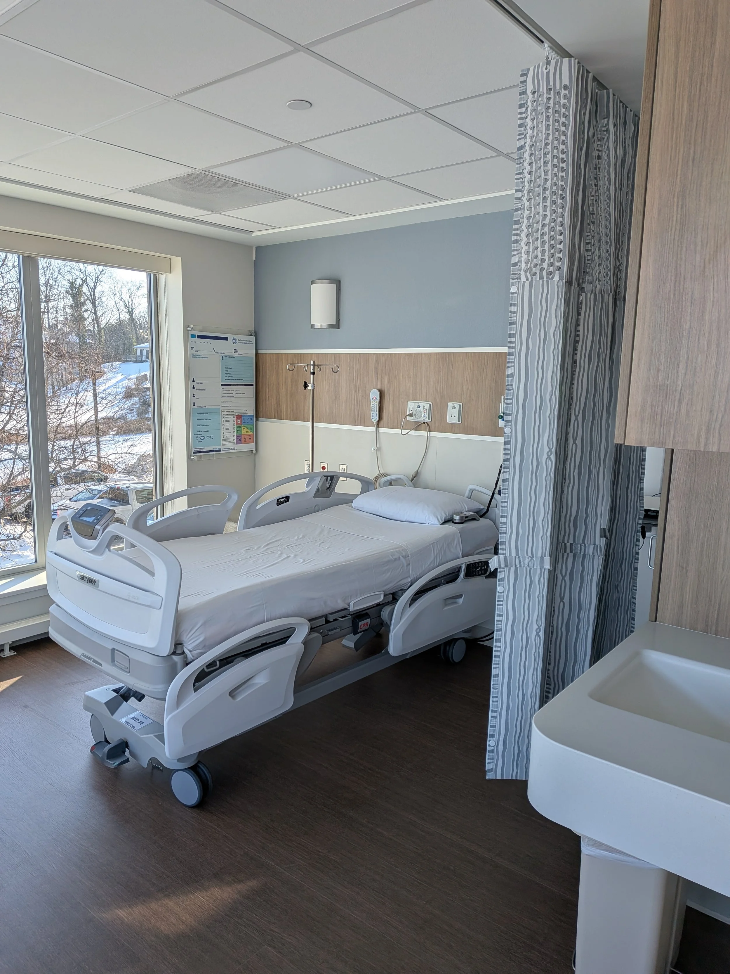 A hospital room with a hospital bed near a window, medical equipment, and a privacy curtain.