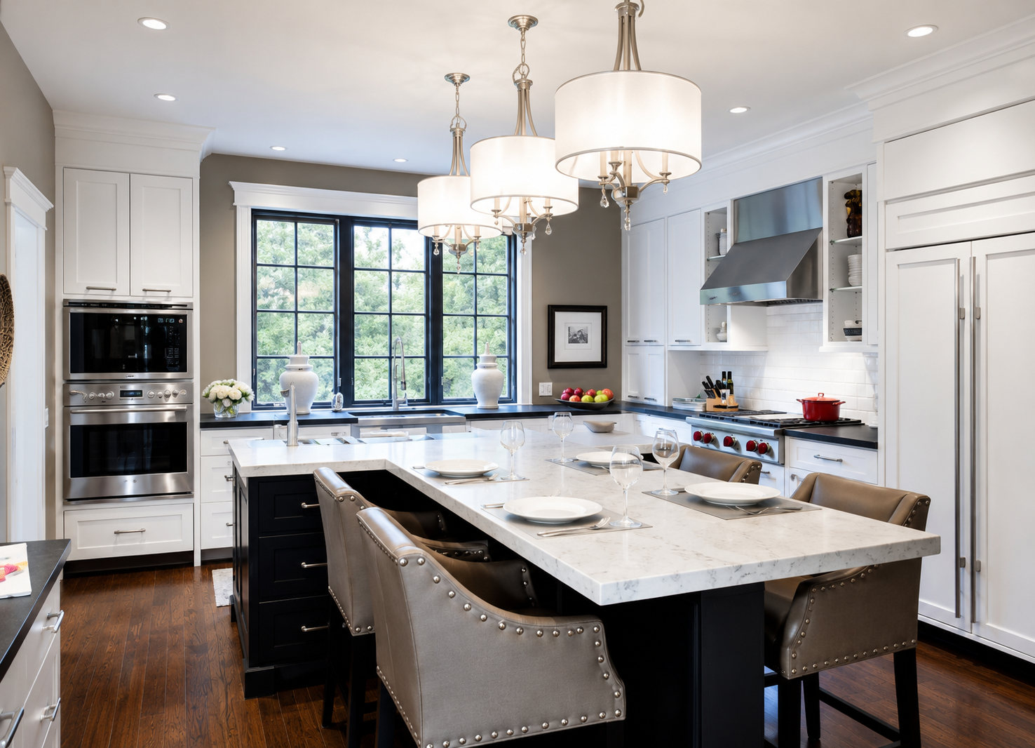 Modern kitchen with white cabinetry, black countertops, stainless steel appliances, and a large island with a marble countertop. There are four pendant lights hanging above the island, and a window with black framing letting in natural light. The tab