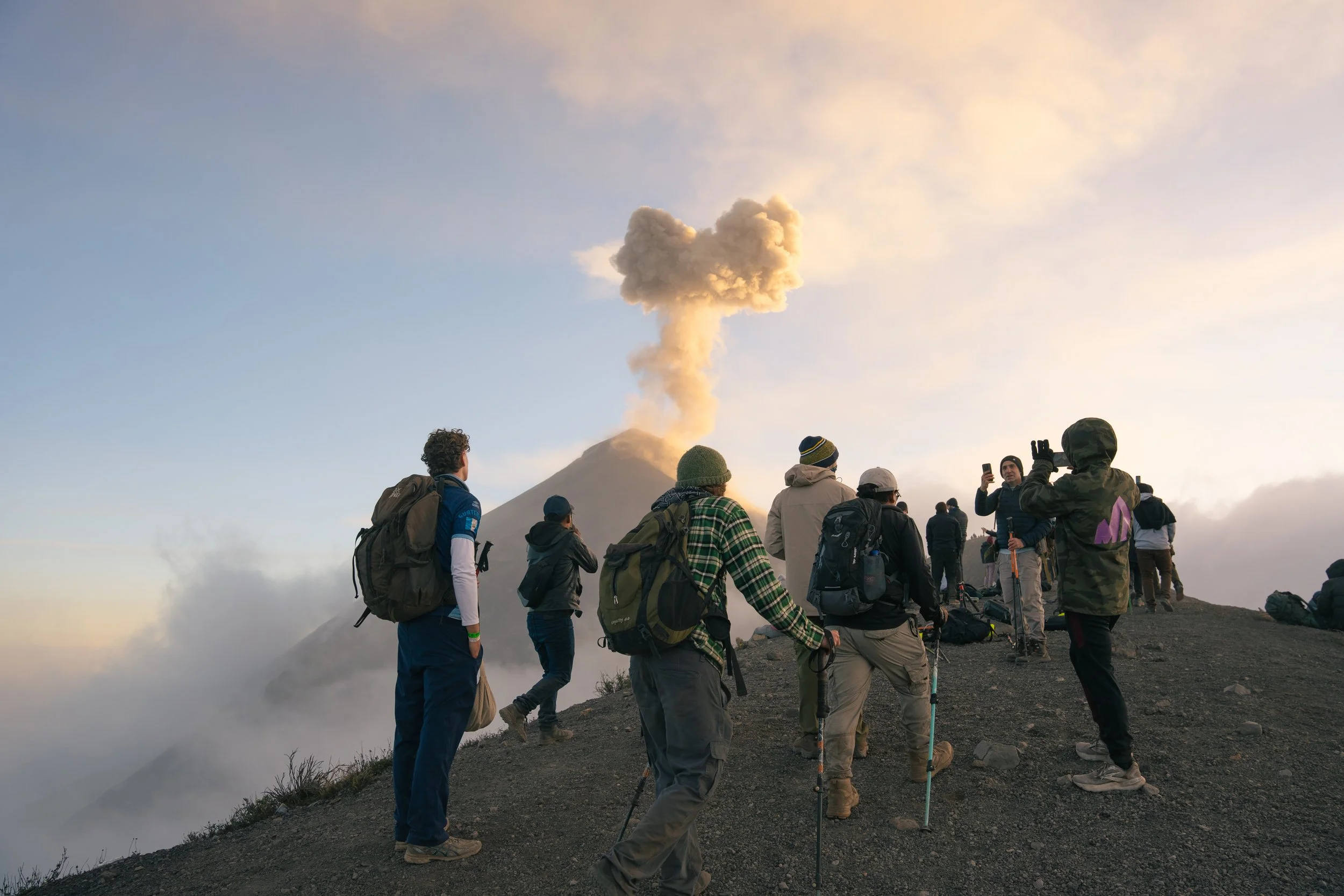 A group of hikers on Volcan de Fuego in Guatemala, viewing the releasing smoke and ash in the sky at sunset.