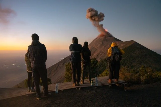 People observing a volcanic eruption at dawn.