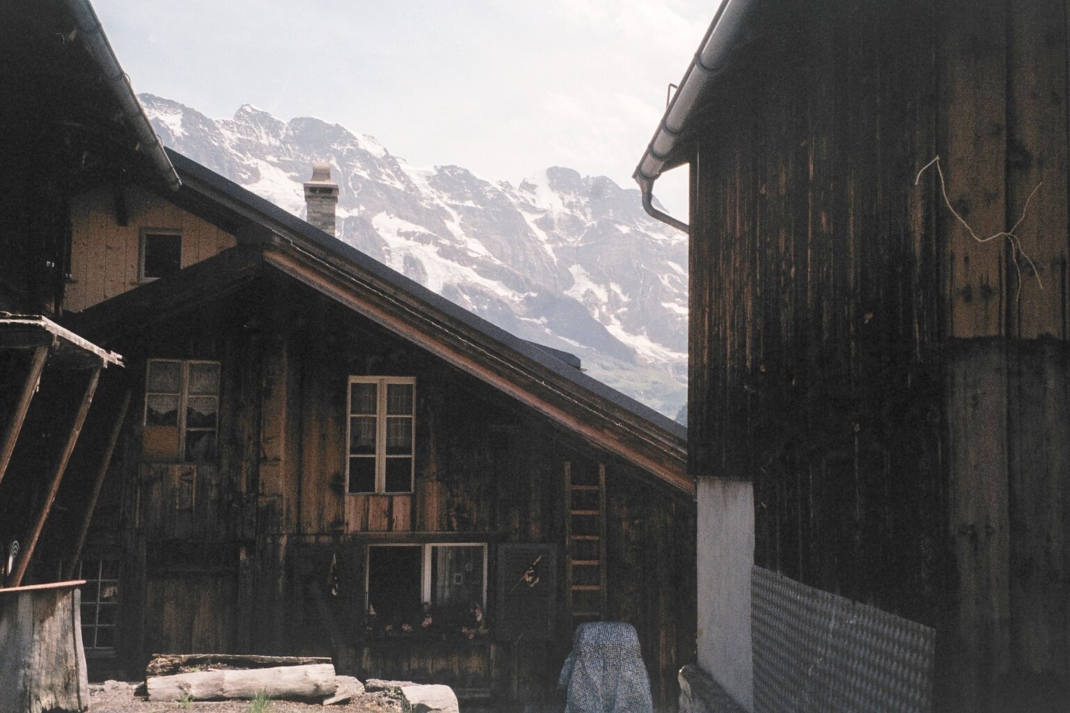 Two rustic wooden houses with snow-capped mountains in the background.