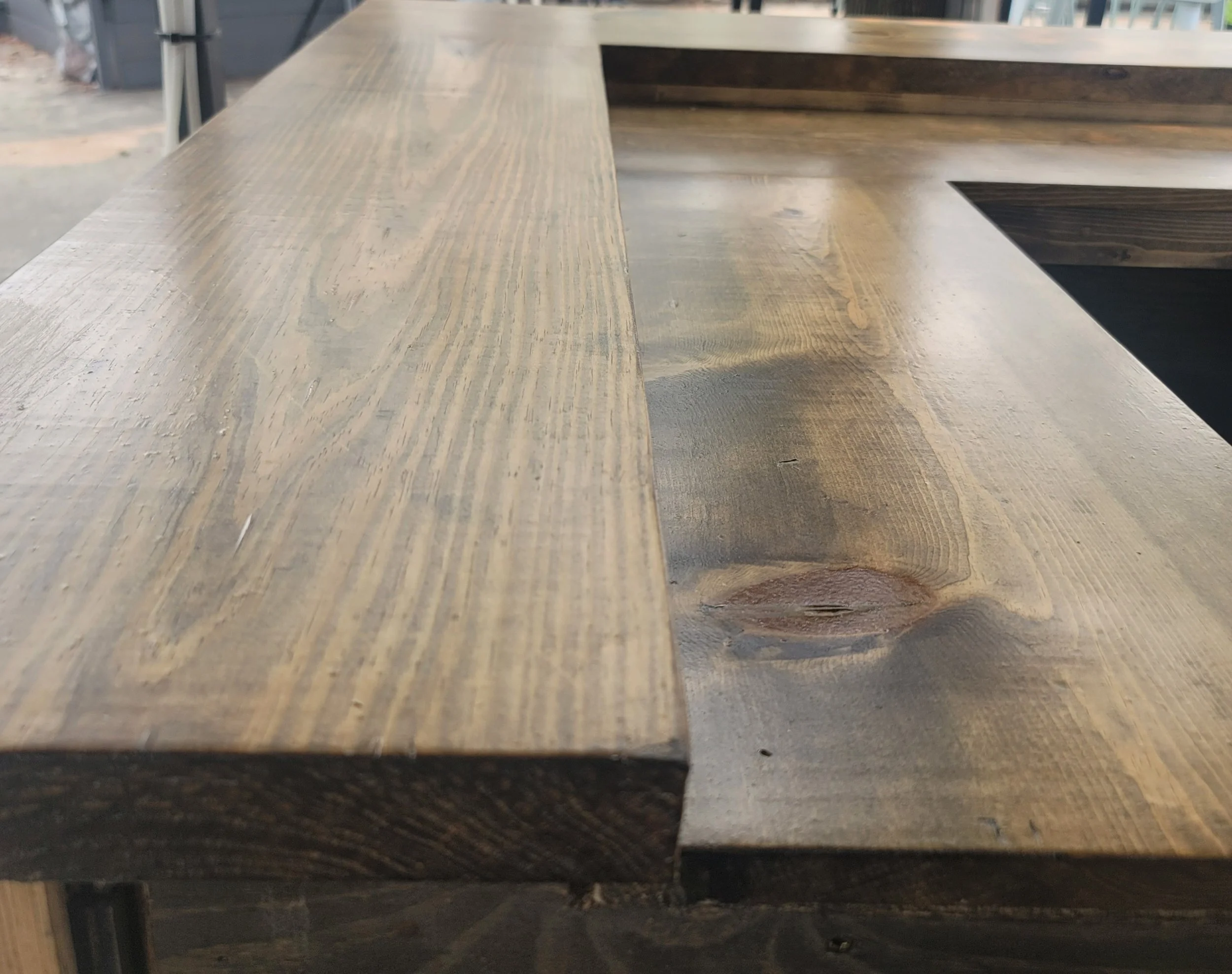 Close-up of a wooden table with a smooth, polished surface and visible wood grain, situated in what appears to be a workshop or industrial space.